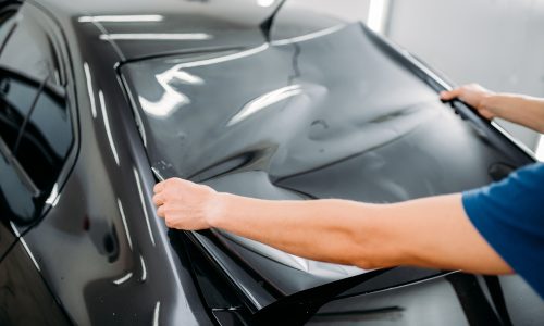 Male specialist with car tinting film in hands. Installation process, tinted auto glass installing procedure